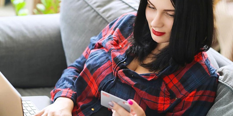 Ragazza mora seduta sul divano che osserva la carta di credito che tiene sulla mano sinistra